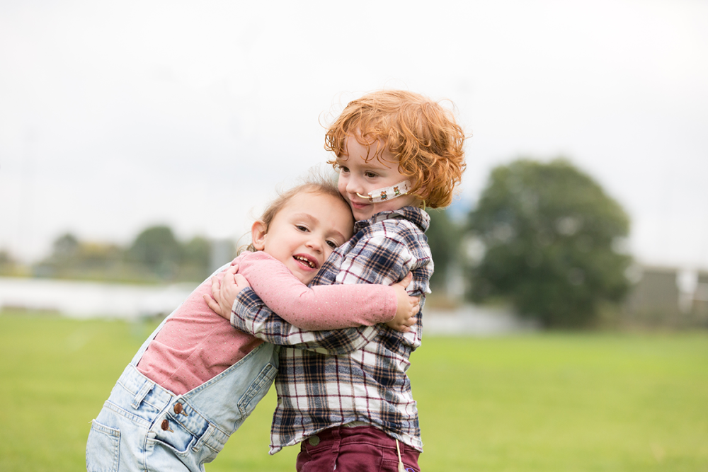 Two young children, a boy (with nasal tube) and girl, hugging