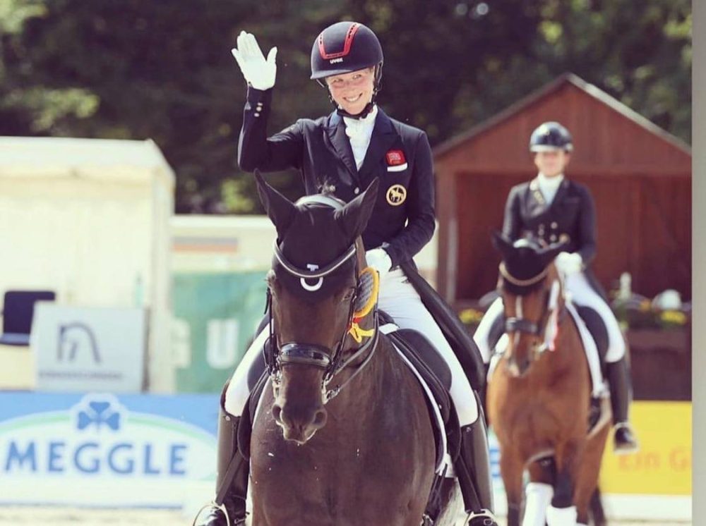 Laura Tomlinson riding one of her horses at a competition and waving to the crowd.